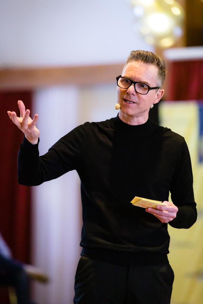 Holger Nitsche speaking on stage, one hand raised in a gesture and cue cards in the other